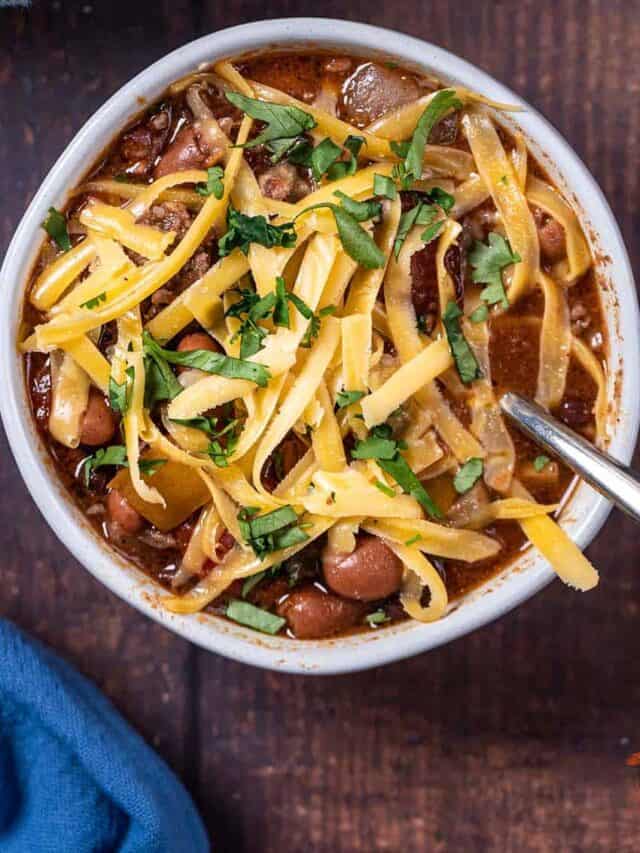 white bowl with beef chili topped with cheese and a spoon