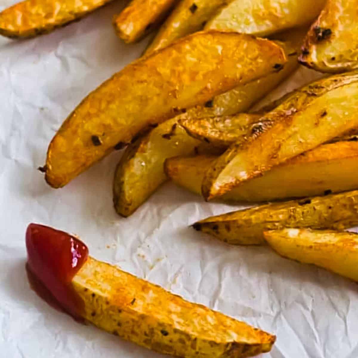 closse up image of steak fries on paper, one dipped in ketchup