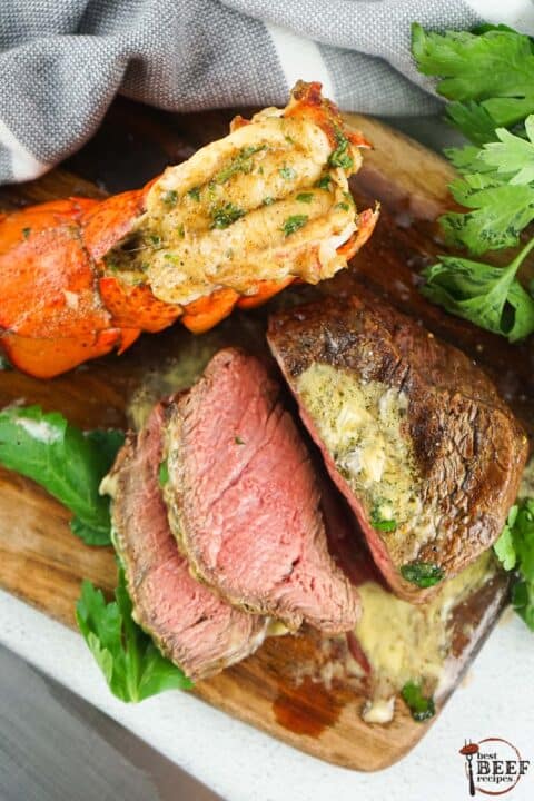 sliced filet mignon on a cutting board with lobster tail and bearnaise sauce