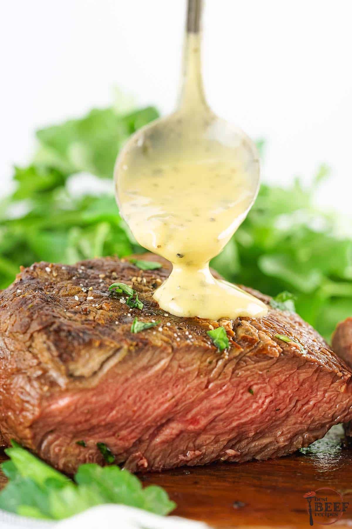 drizzling bearnaise sauce over sliced filet mignon on a cutting board