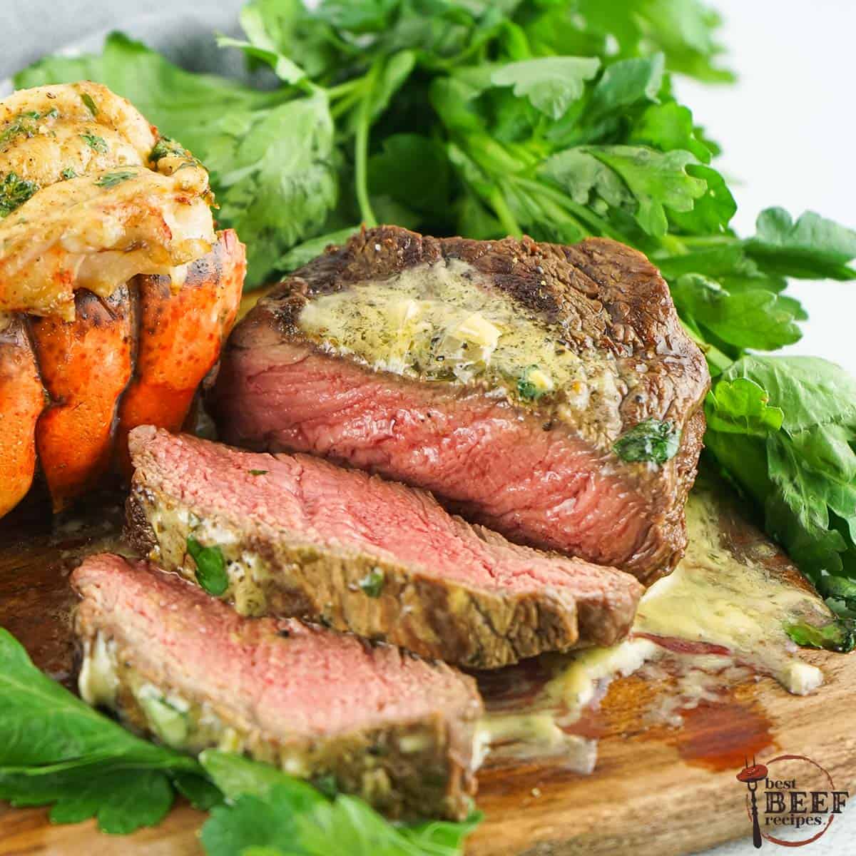 sliced filet mignon steak with bearnaise sauce up close on a cutting board with lobster tail