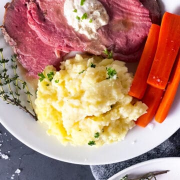 prime rib sliced on a plate with steak mashed potatoes, and carrots