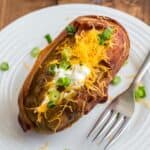 steakhouse baked potato up close stuffed with cheese, green onions and green onions, and wrapped in bacon