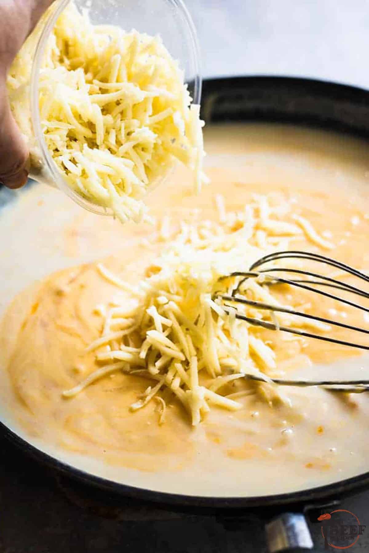 adding cheese into a saucepan for steakhouse mac and cheese