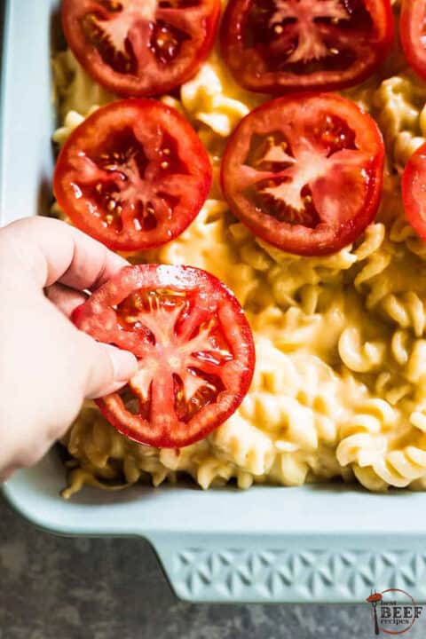 adding sliced tomatoes on top of steakhouse mac and cheese before baking