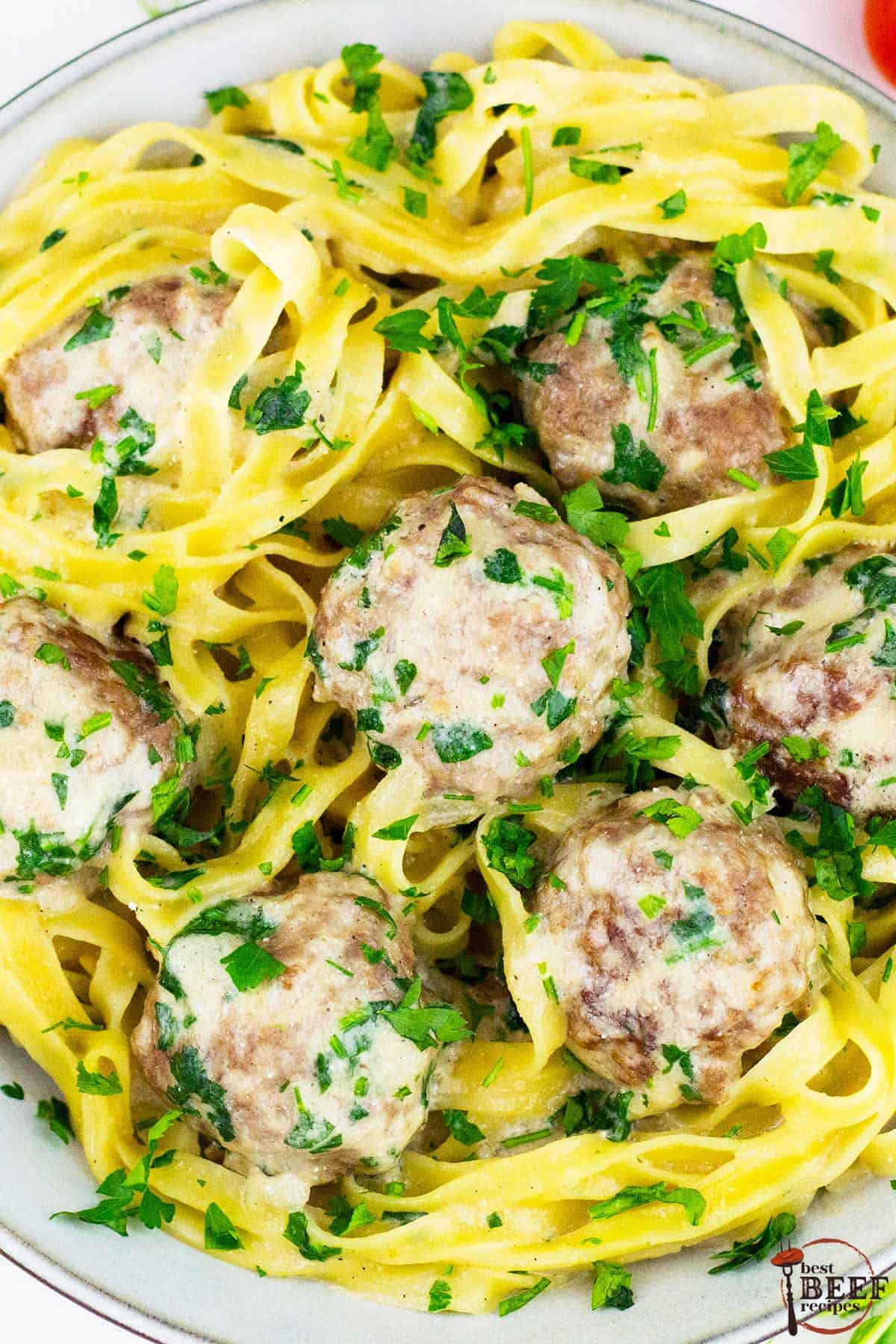 a top down view of a plate of swedish meatballs on a bed of egg noodles, sauce and parsley