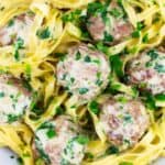 a closeup of swedfish meatballs garnished with parsley on a bed of egg noodles and sauce