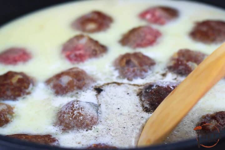 swedish meatball sauce being stirred in a pan full of meatballs with a wooden spoon