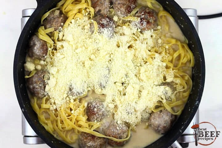 a top view of a cast iron pan with swedish meatballs, cooked egg noodles and sauce, covered in parmesan cheese