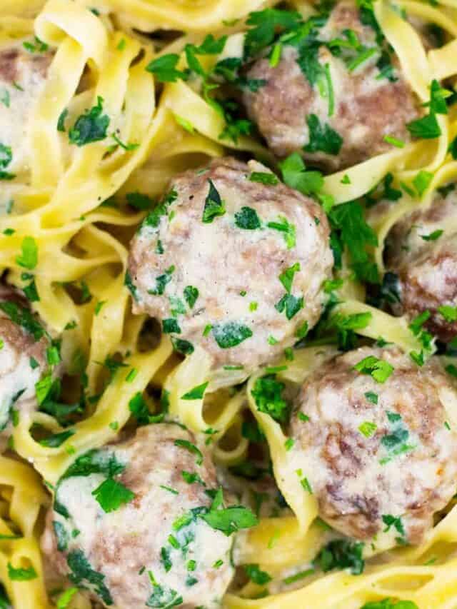 a closeup of swedfish meatballs garnished with parsley on a bed of egg noodles and sauce
