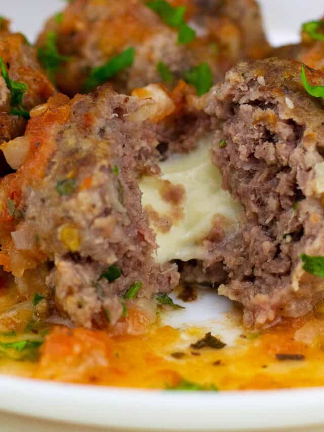 a closeup of a plate full of stuffed meatballs where the front meatball has been split to show the cheese