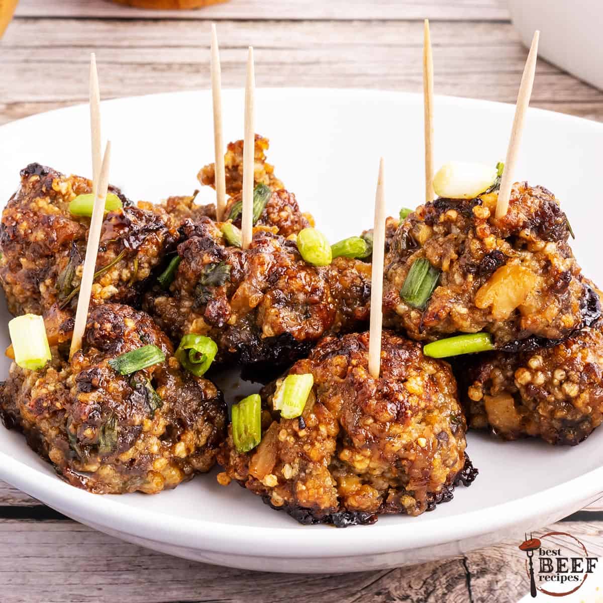 a white plate full of baked hoisin meatballs with toothpicks