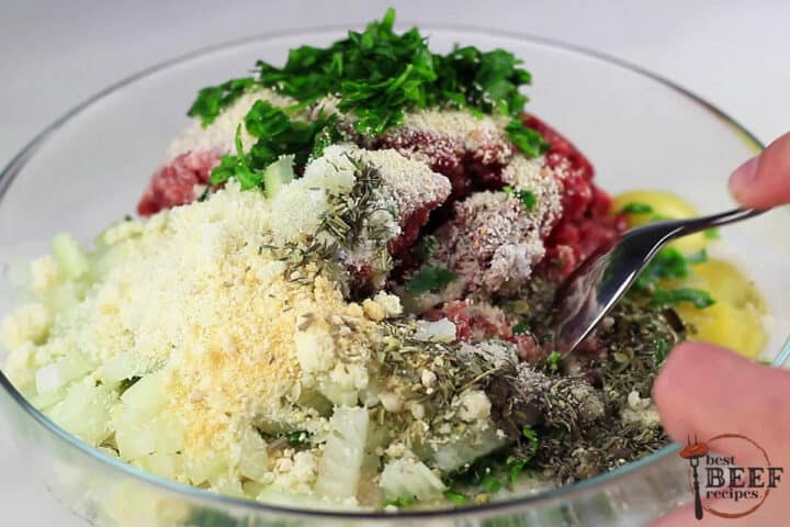 a glass bowl filled with meatball mixture ingredients being mixed with a spoon