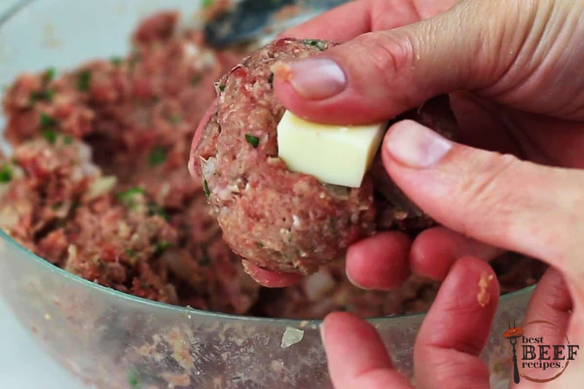 hands pressing a piece of mozzarella into a meatball over a dish of meatball mixture