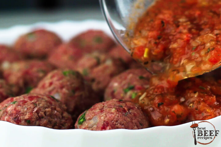 tomato sauce being poured on a dish of raw stuffed meatballs