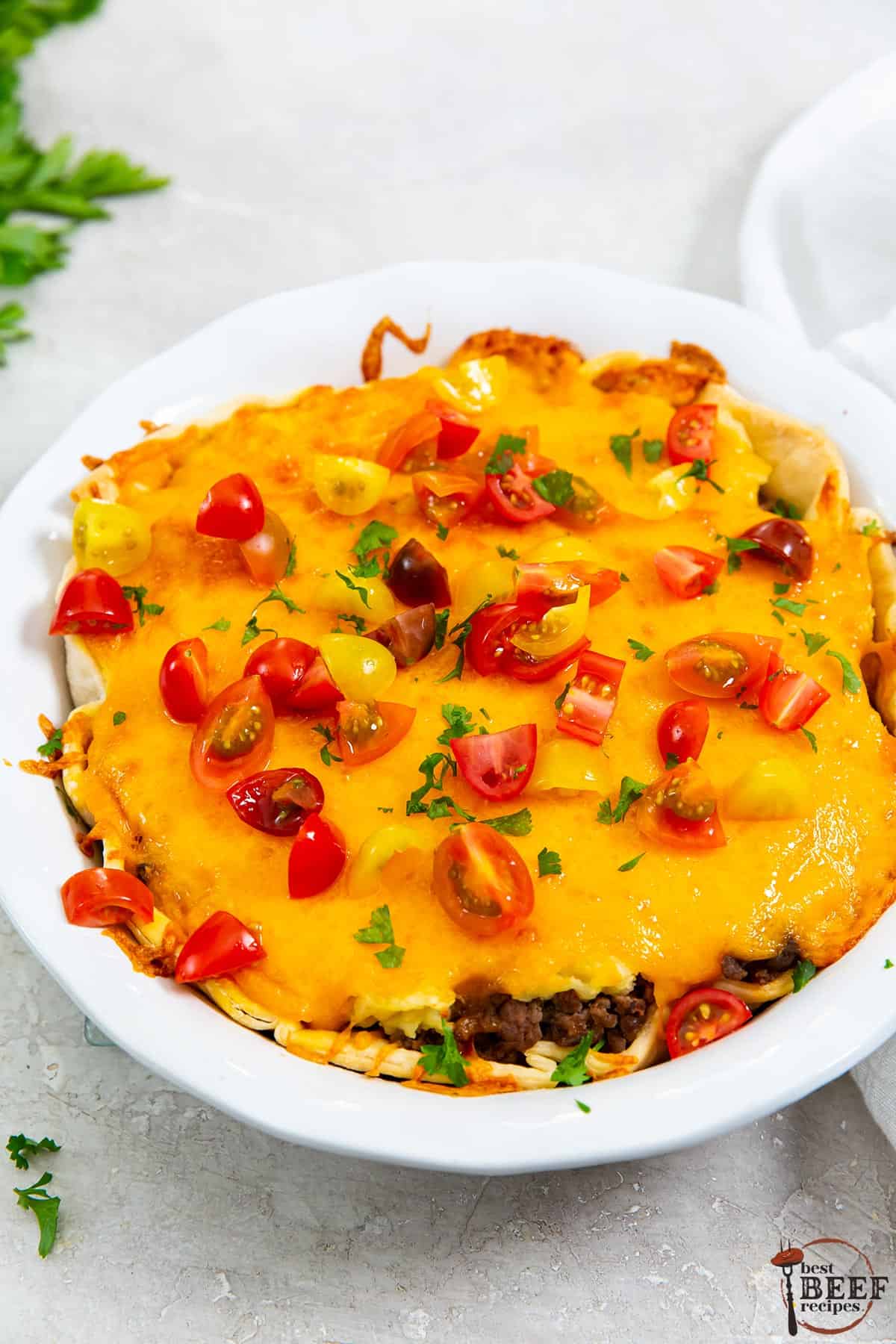 baked cheeseburger pie in a dish with sliced tomatoes and parsley for garnish