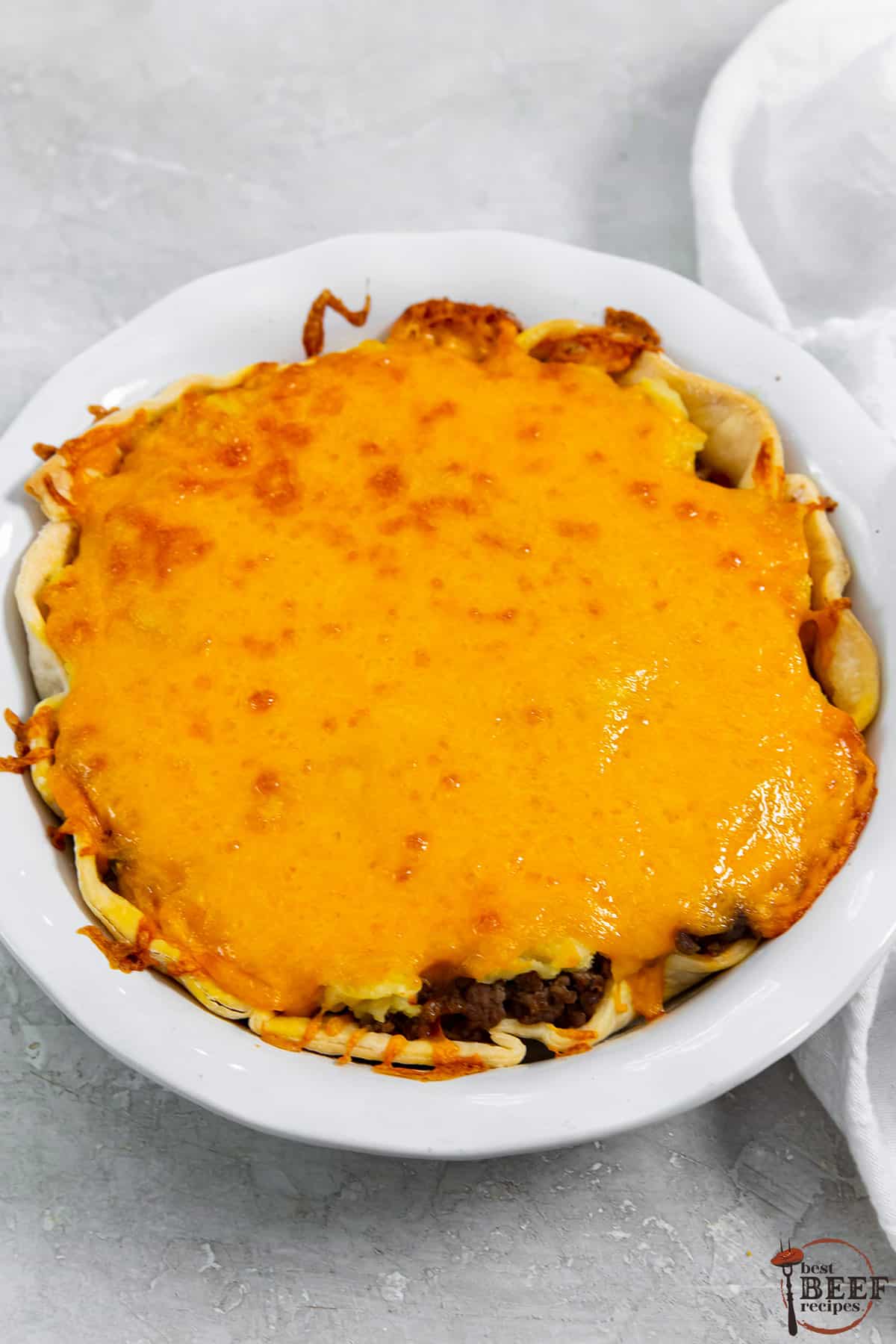 a fully baked cheeseburger pie in a white pie dish with melted cheese