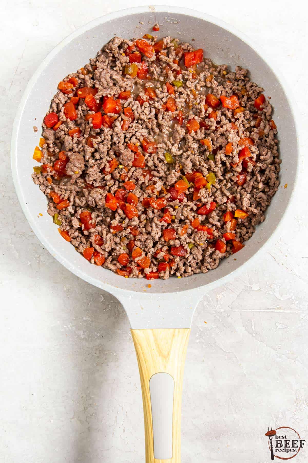 browned ground beef, tomatoes, and green chilies in a frying pan on a counter