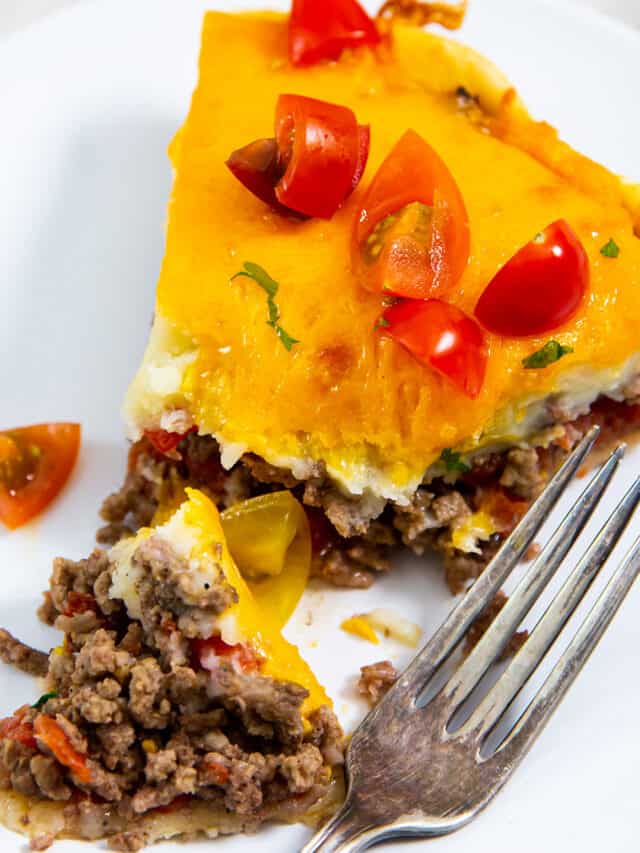 a closeup of a slice of cheeseburger pie on a white plate with a fork