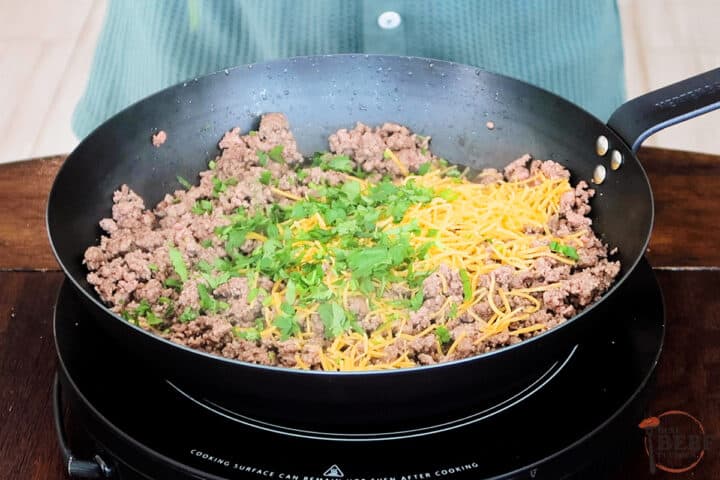 adding cheese and cilantro to browned ground beef