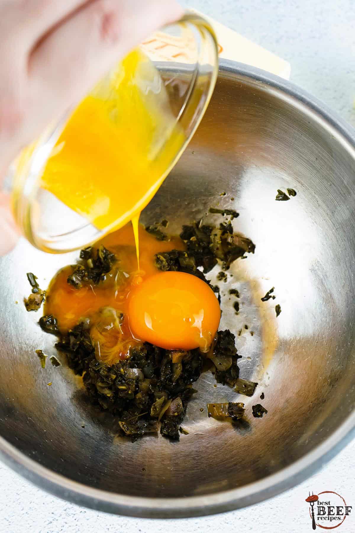egg yolks being added to a metal bowl full of reduced oil and herbs