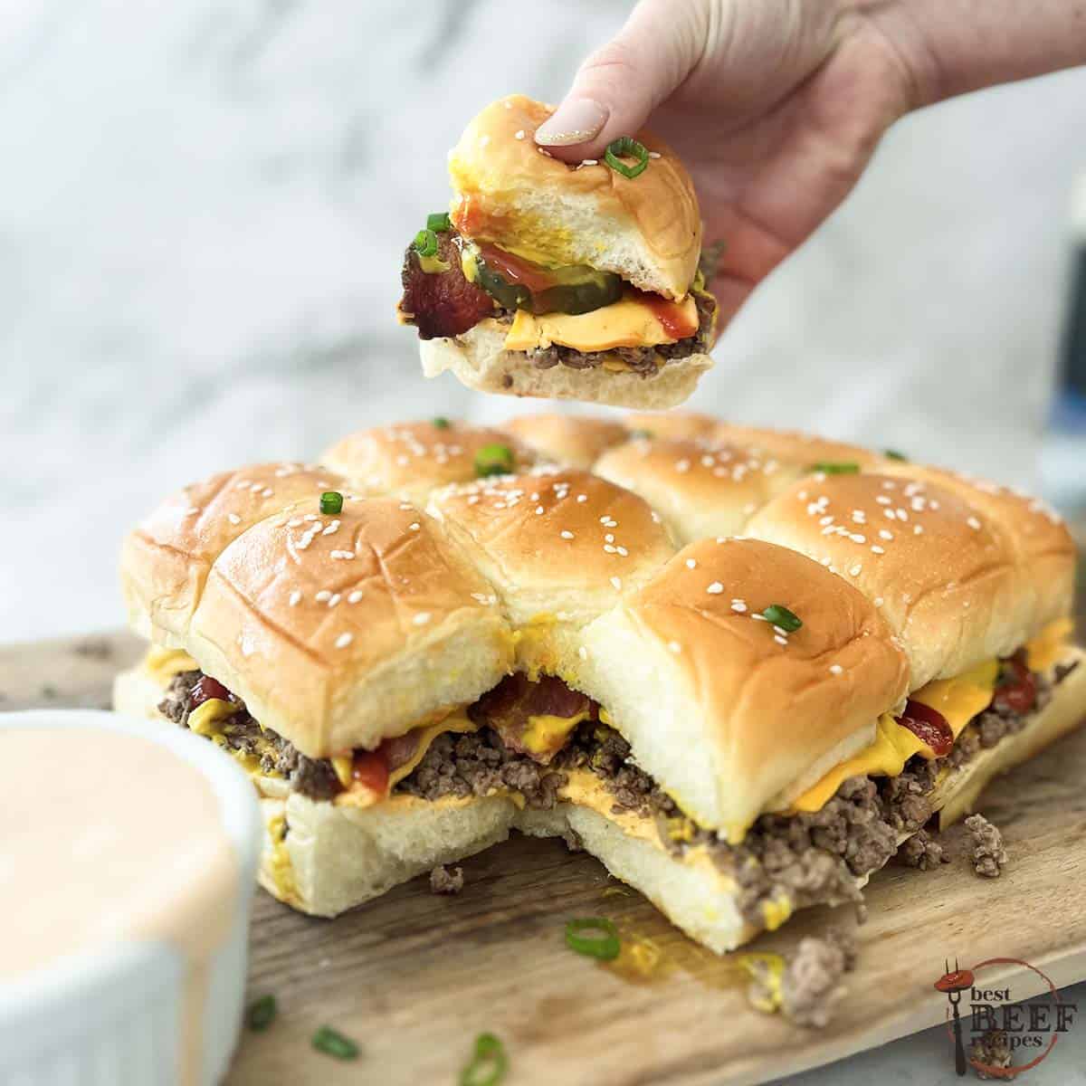 lifting a cheeseburger slider over the other sliders with a side of burger sauce