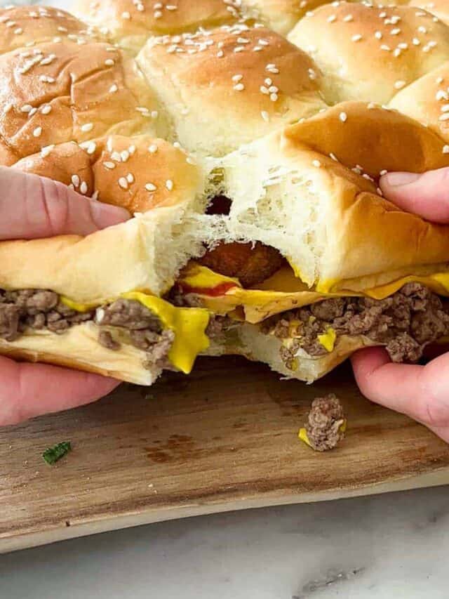 pulling apart cheeseburger sliders on a wooden serving board