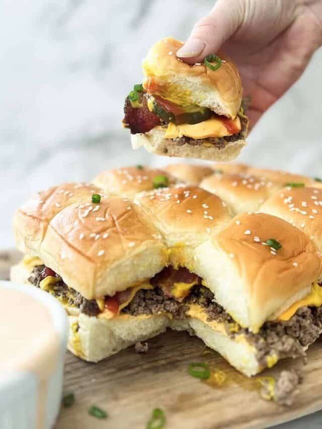 lifting a cheeseburger slider over the other sliders with a side of burger sauce