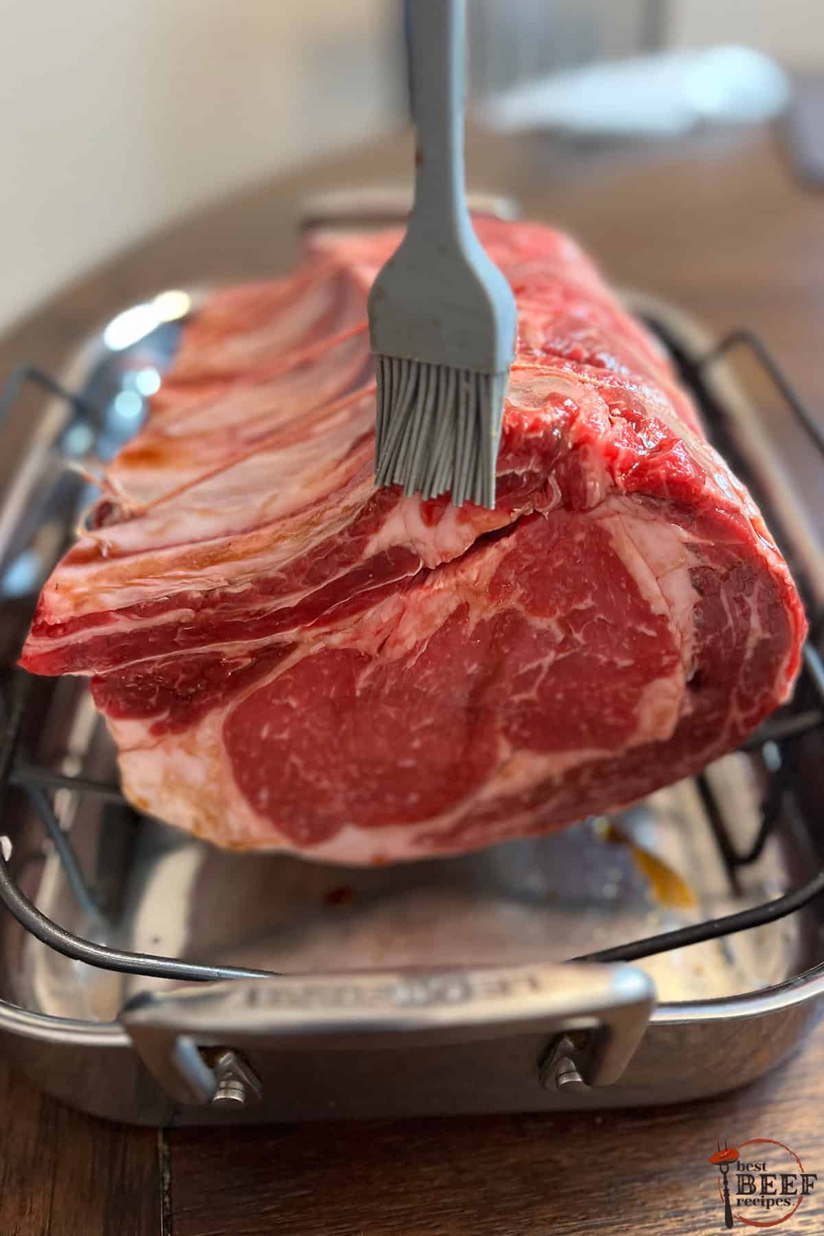 soy sauce being brushed on prime rib over a roasting pan