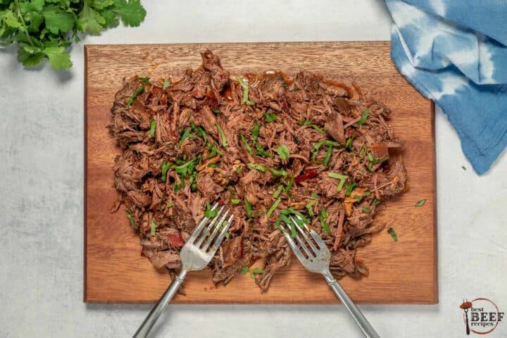 barbacoa being shredded on a cutting board with two forks