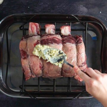 adding garlic prime rib butter rub to a prime rib with the back of a spoon