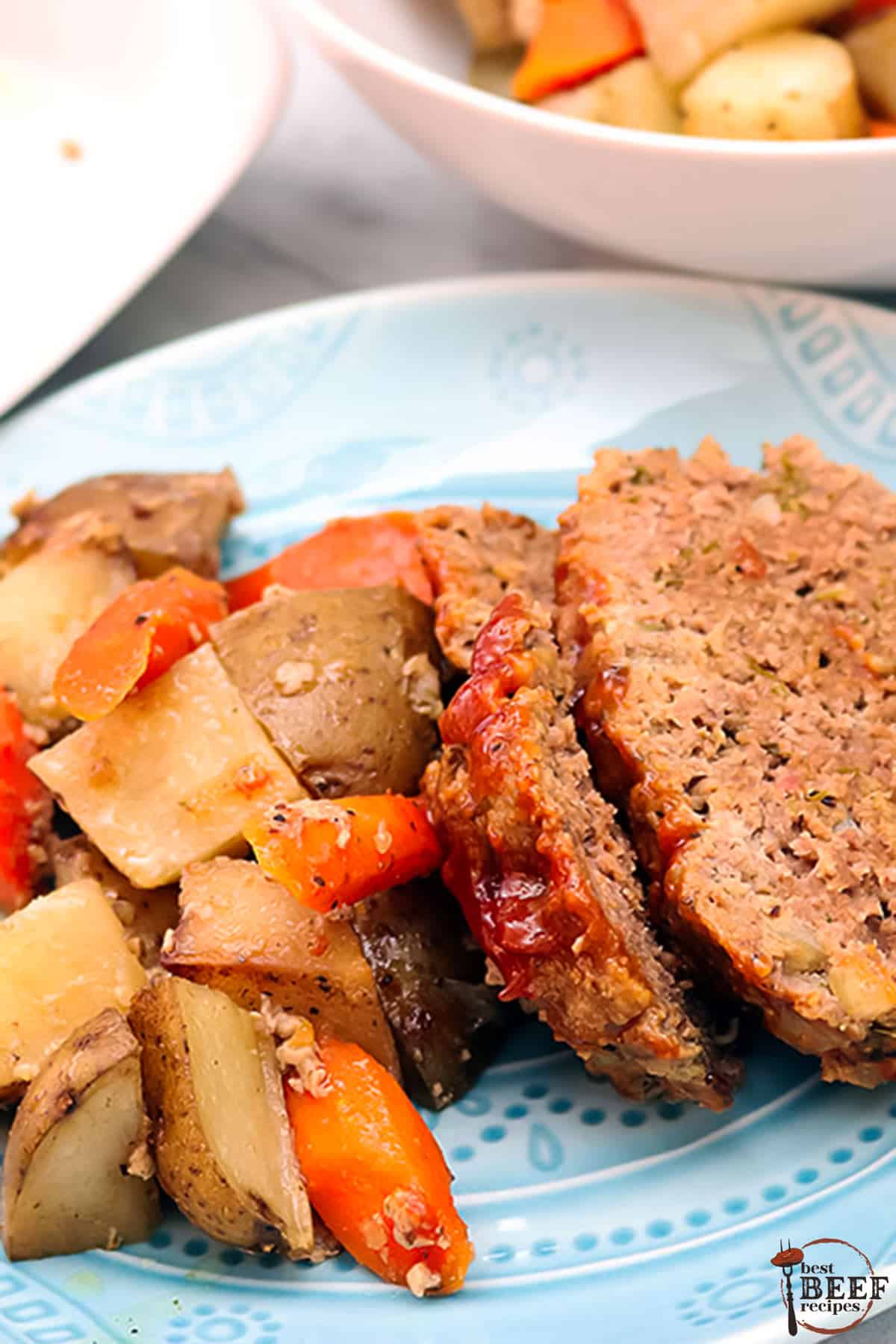 a plate filled with slices of slow cooker meatloaf, carrots, and potatoes