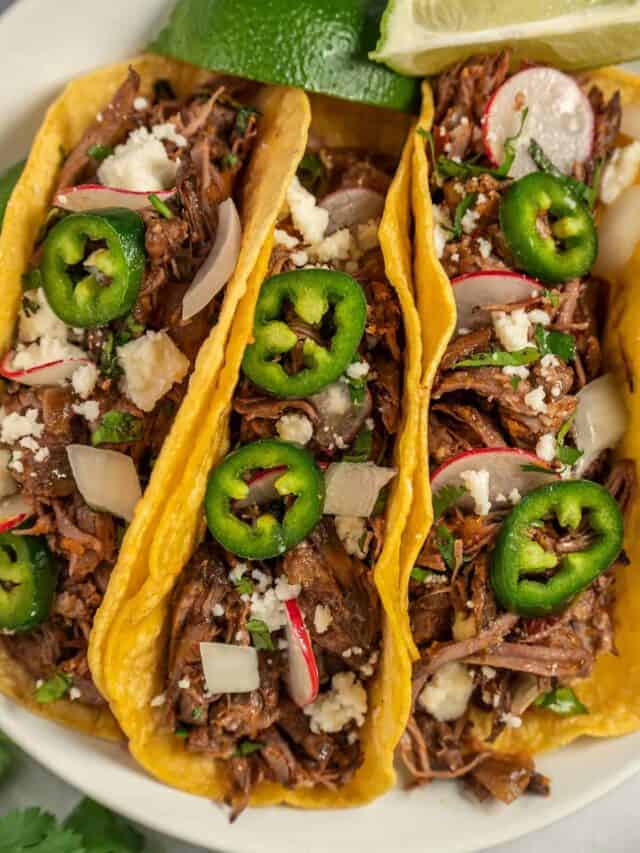 a plate stuffed with three filled barbacoa tacos and lime slices