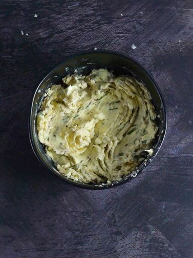 prime rib butter rub mixed in a small black bowl next to garlic bulbs