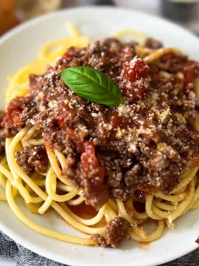 a plate of sugo di carne on spaghetti with a basil leaf garnish