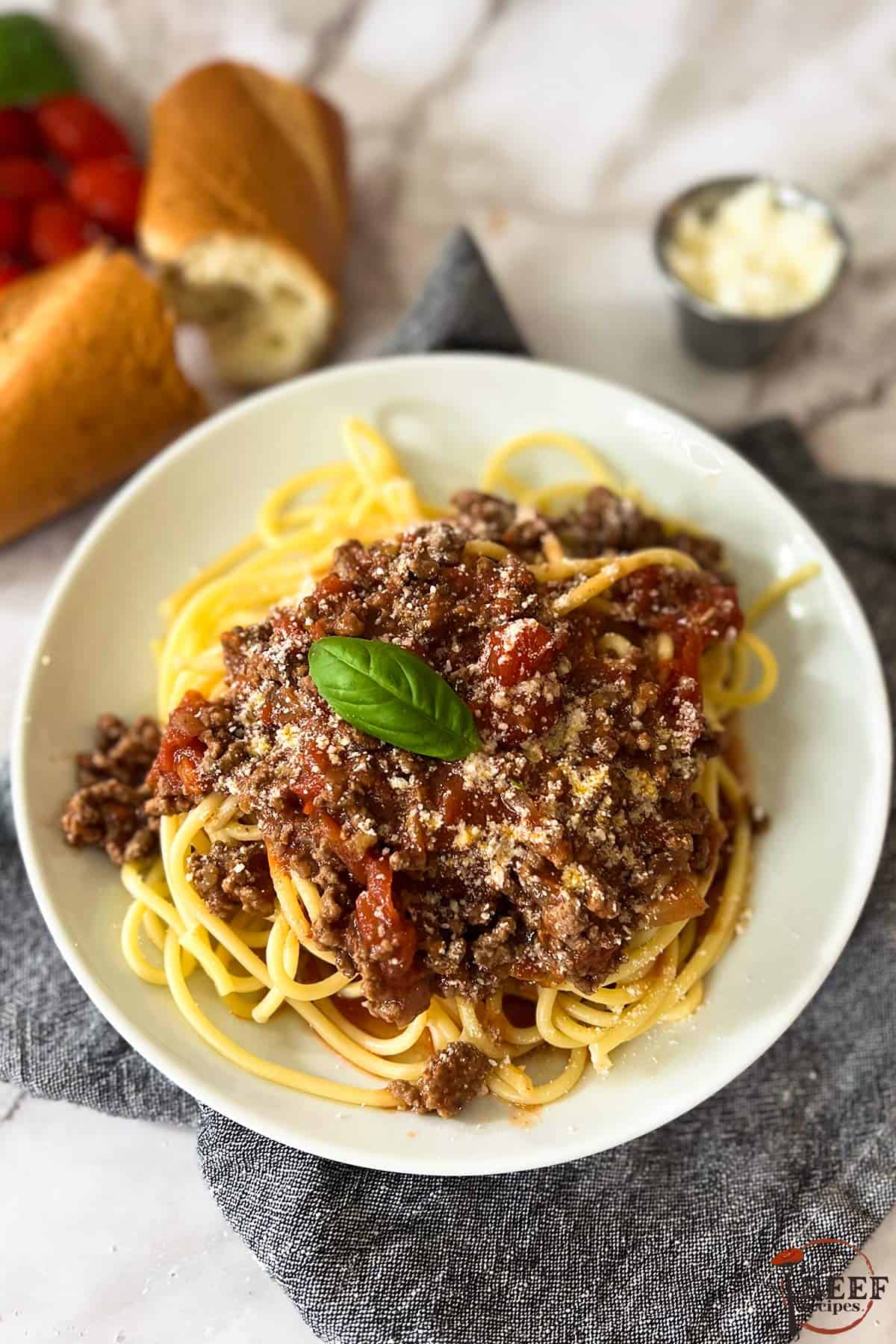 sugo di carne and spaghetti on a plate with a bread roll in the background