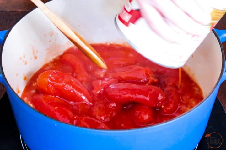 a can of peeled tomatoes being added to the pot