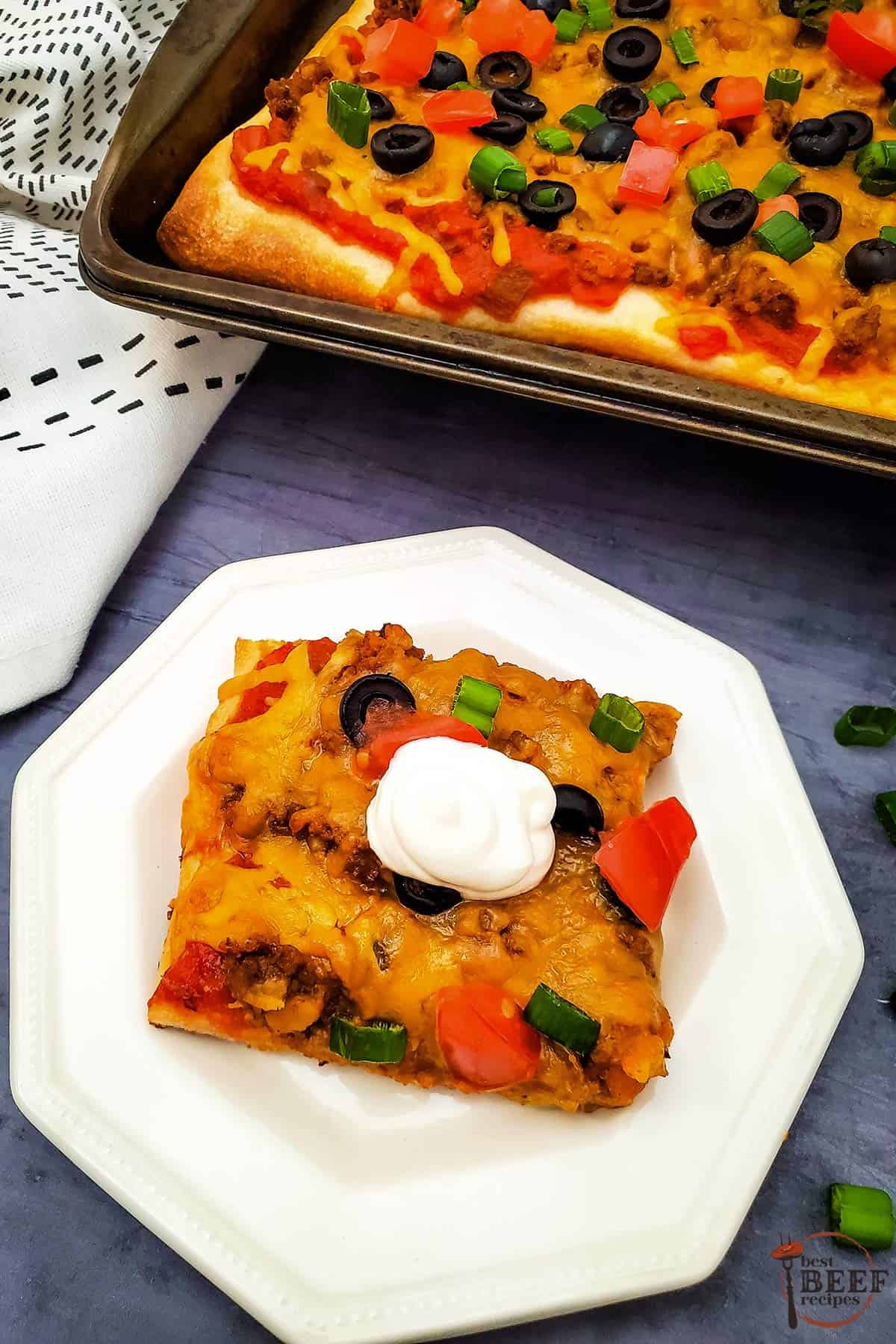 taco pizza on a white plate next to a sheet pan of taco pizza