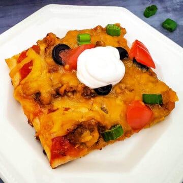 a completed slice of taco pizza on a white plate with a spoonfull of sour cream on top