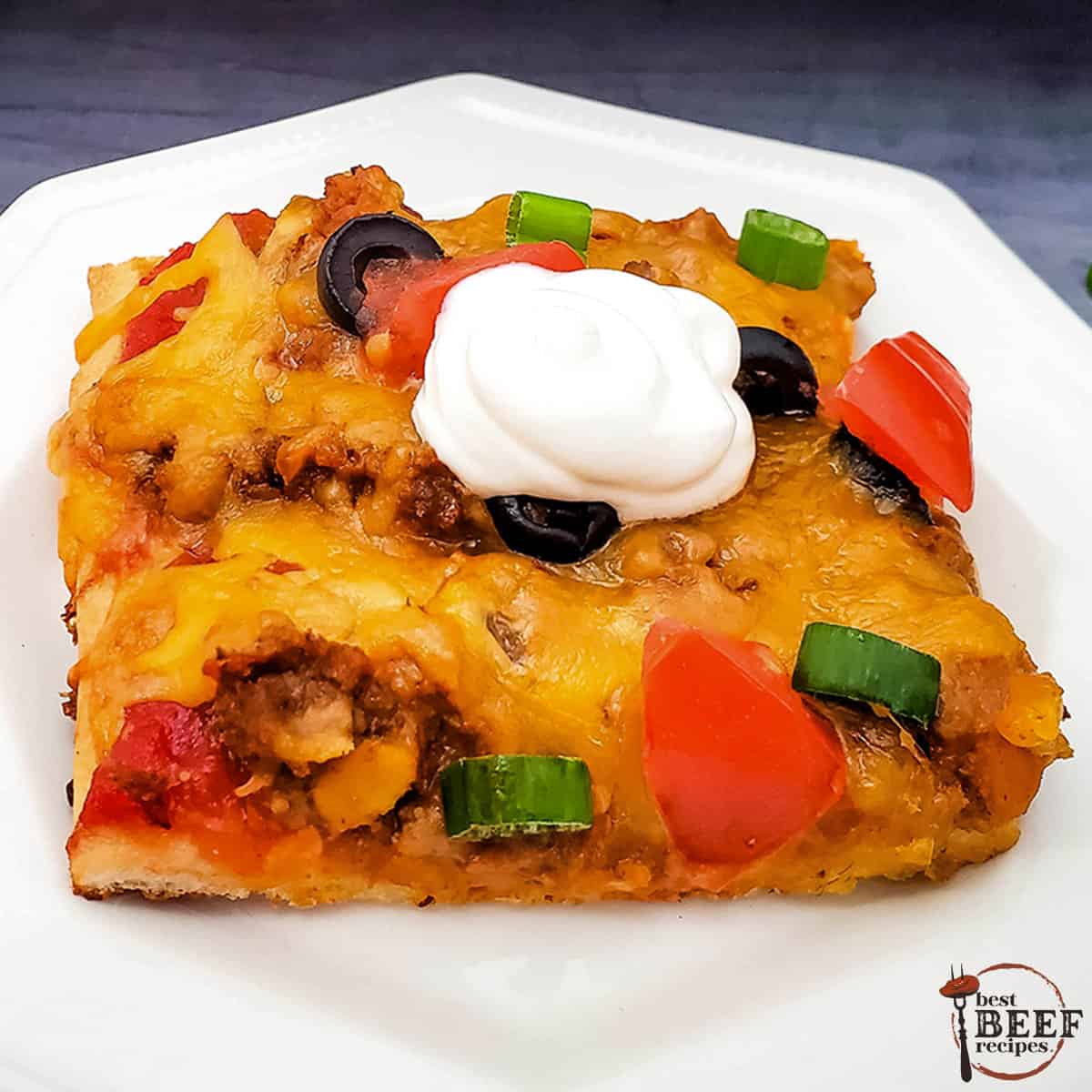 A slice of taco pizza on a white plate with a dollop of sour cream