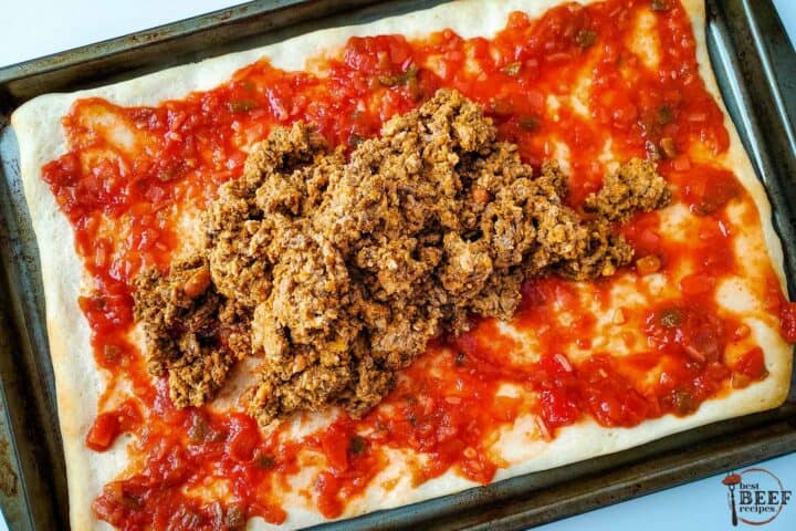 beef and beans being spread over a pizza crust with salsa
