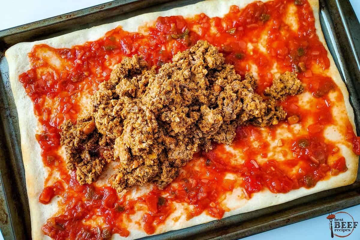 beef and beans being spread over a pizza crust with salsa