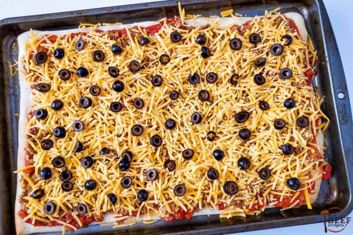 taco pizza covered in cheese and olives before being baked