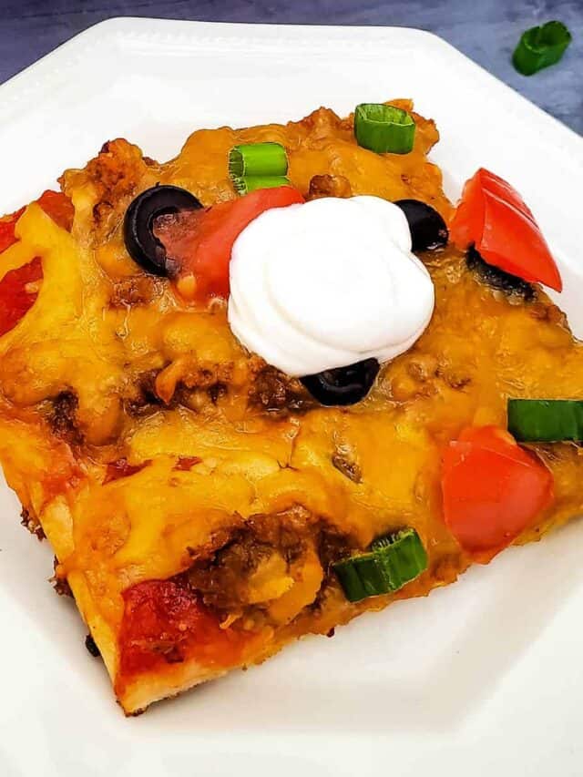a completed slice of taco pizza on a white plate with a spoonfull of sour cream on top