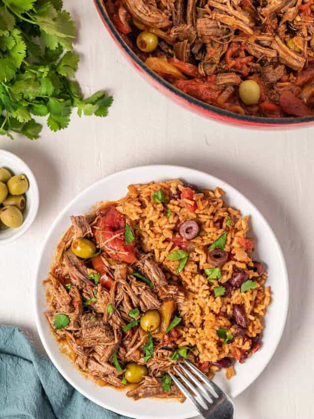 a dinner spread of a plate of ropa vieja, beans and rice, olives, and a pot of more ropa vieja