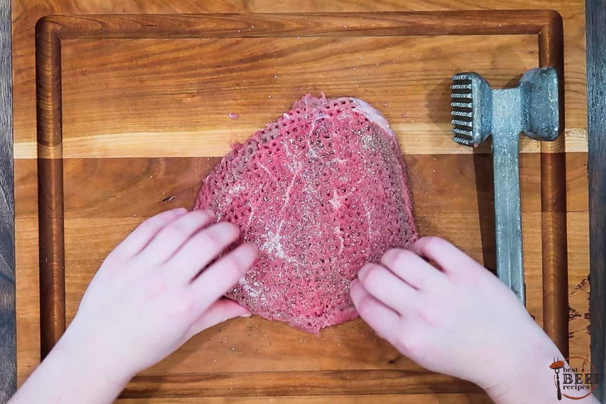 tenderized steak with added seasonings on a cutting board