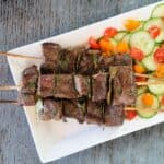 grilled beef kabobs on a white plate with vegetables