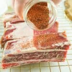 seasonings in a jar being poured over slices of beef