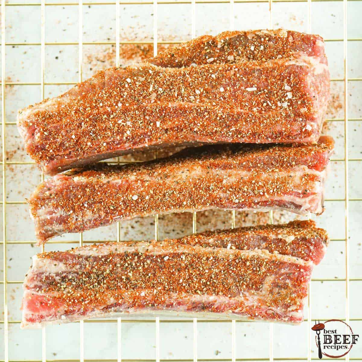 a row of uncooked beef ribs on a wire rack covered in seasonings