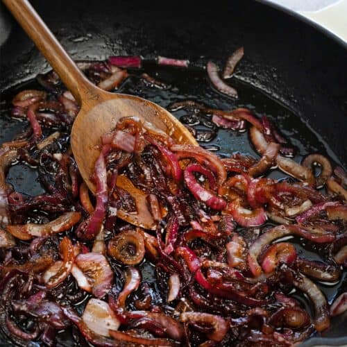 caramelized onions for burgers in a black skillet with a wooden spoon